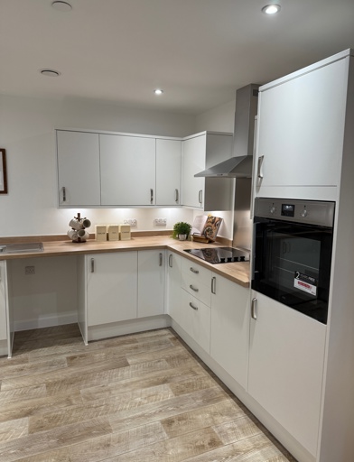 A kitchen with wooden flooring, white cupboards with an integrated oven and hob with wooden counter tops  