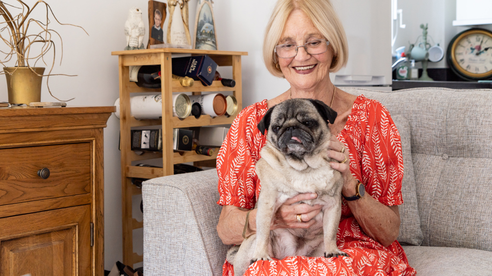 Resident in a red dress sat on a sofa in their apartment with pet dog on their lap