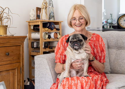 Resident in a red dress sat on a sofa in their apartment with pet dog on their lap