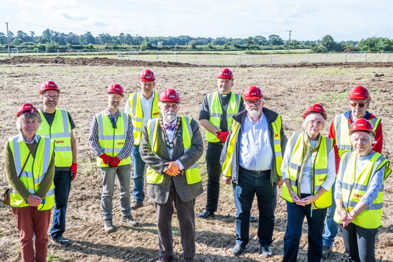 Employees of Housing 21 along with special guests wearing high-vis jackets and hard hats standing outside.