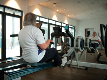 A female resident using the rowing machine in the gym at Lime Gardens