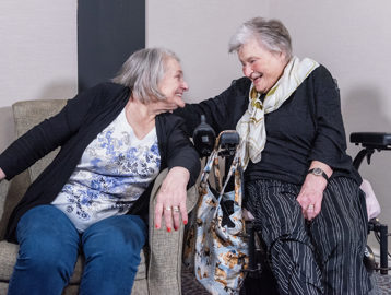Two residents sitting in a living room facing each other and laughing