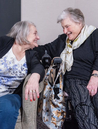 Two residents sitting in a living room facing each other and laughing