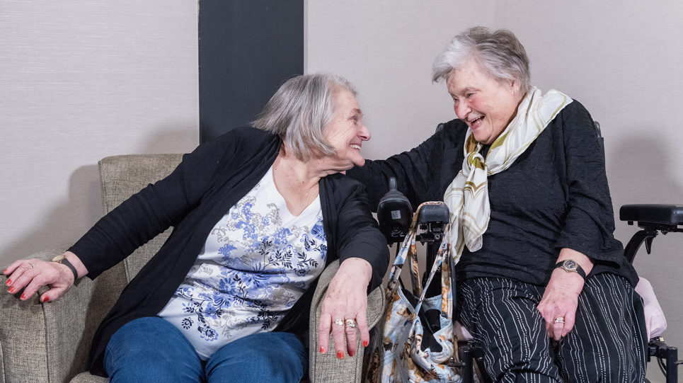Two residents sitting in a living room facing each other and laughing
