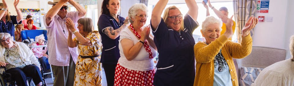 Residents and carers dancing in a communal lounge 