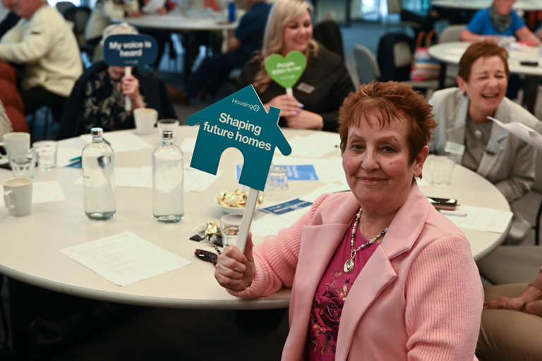 A resident with red hair and a pink jacket, holding an influencer sign, smiling