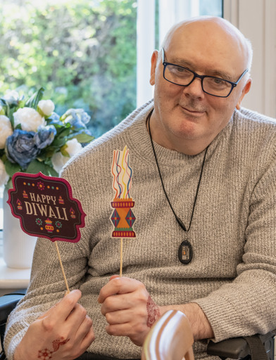 Resident in a wheelchair smiles and holds Happy Diwali themed props 