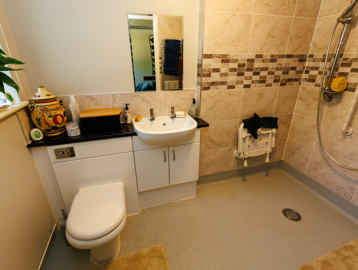 Bathroom showing a walk-in shower, toilet, and sink basin, with tiled walls in a sandy colour.