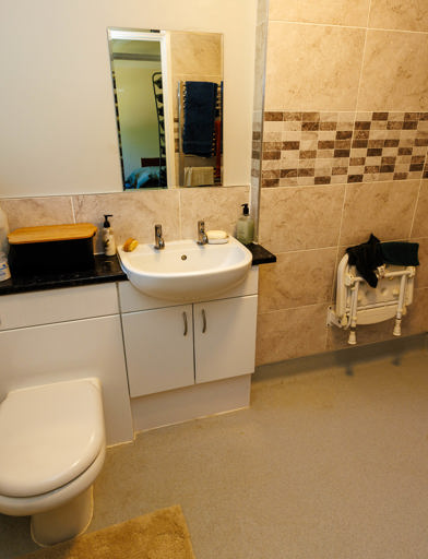 Bathroom showing a walk-in shower, toilet, and sink basin, with tiled walls in a sandy colour. 