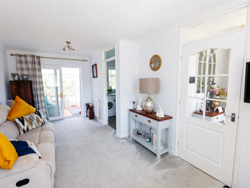 A lightly-decorated living room with window, sofa, TV and furniture and doors leading to a conservatory, kitchen and hallway