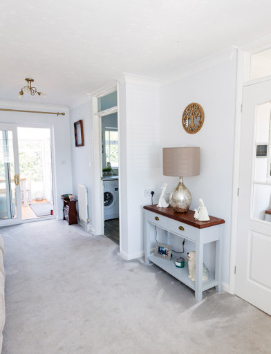 A lightly-decorated living room with window, sofa, TV and furniture and doors leading to a conservatory, kitchen and hallway 