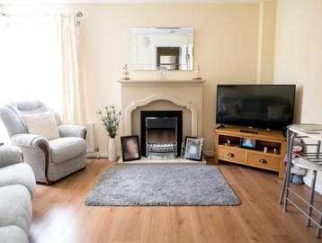 A living room with television, mantlepiece, sofas and large window