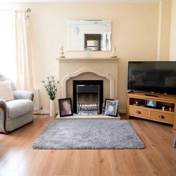 A living room with television, mantlepiece, sofas and large window