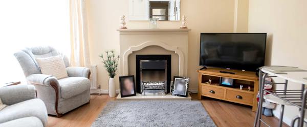 A living room with television, mantlepiece, sofas and large window