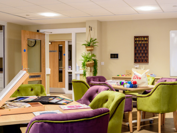 Activity room for residents with soft seating and modern purple and green decor