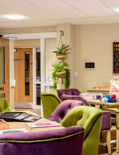Activity room for residents with soft seating and modern purple and green decor 