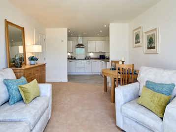 An open plan kitchen and living room furnished with a sofa, arm chair, dining table and sideboard 