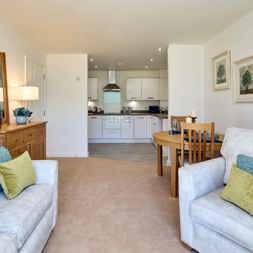 An open plan kitchen and living room furnished with a sofa, arm chair, dining table and sideboard
