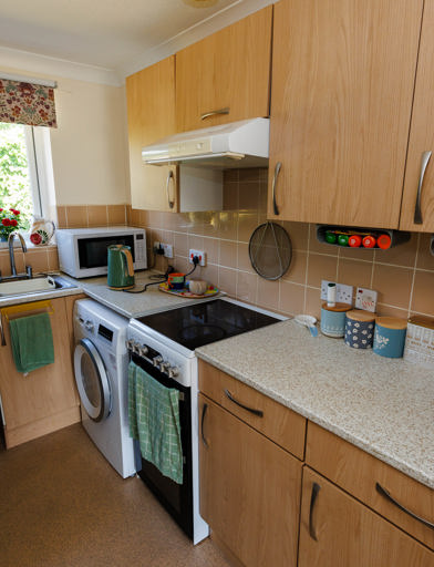 Kitchen with fitted units, storage space, washing machine, small double oven, and window overlooking the garden 