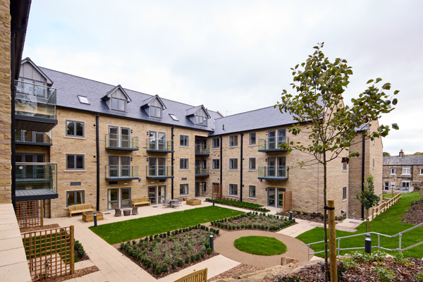 The exterior of a four-storey building with balconies overlooking gardens, outdoor paving and a lawn