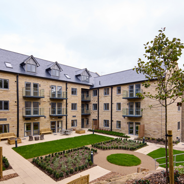 The exterior of a four-storey building with balconies overlooking gardens, outdoor paving and a lawn