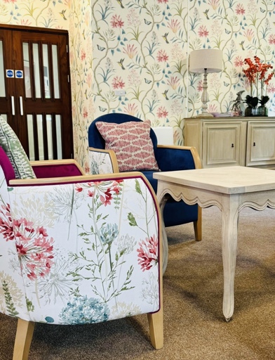 Communal lounge with floral decorated arm chair and wallpaper 