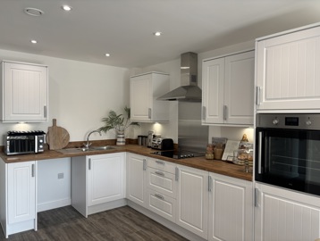 A kitchen with white cupboards featuring brown wooden flooring and a brown counter top