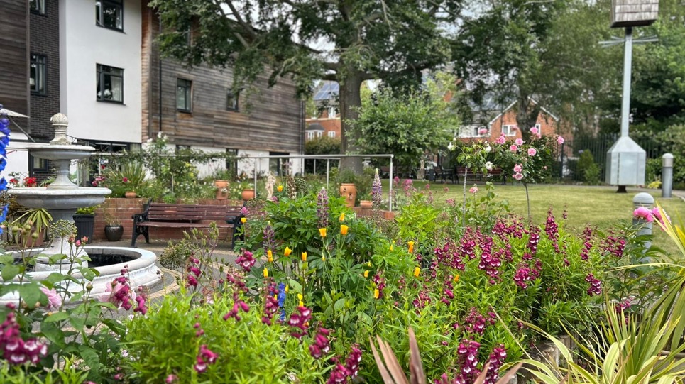 A close up photograph of the flowers and plants in the rear garden with water fountain and seating