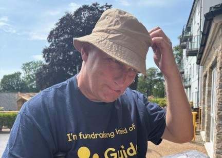 Lee wears a branded Guide Dogs t-shirt and scratches his head in mock confusion pretending to look at a map
