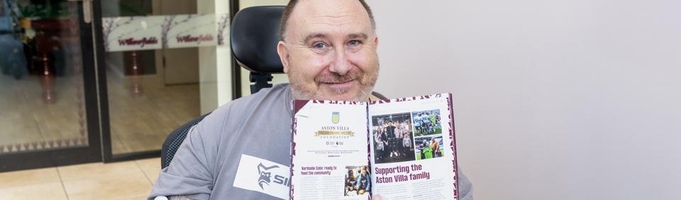 Chris, a Housing 21 resident, holds an Aston Villa programme up to the camera showing an article in which he is featured 