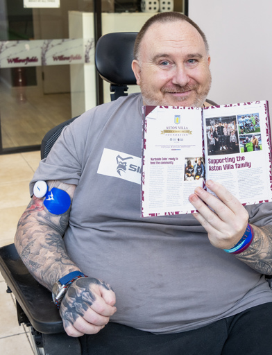 Chris, a Housing 21 resident, holds an Aston Villa programme up to the camera showing an article in which he is featured 