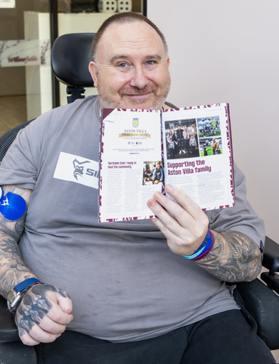 Chris, a Housing 21 resident, holds an Aston Villa programme up to the camera showing an article in which he is featured 
