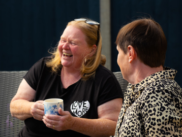 Two residents laughing and enjoying a hot drink in the garden