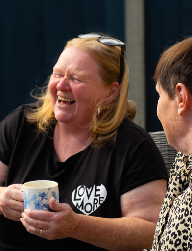 Two residents laughing and enjoying a hot drink in the garden 