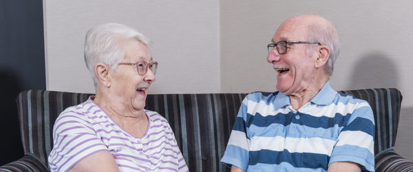 A couple facing each other and laughing on a sofa whilst holding hands 