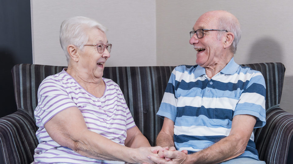A couple facing each other and laughing on a sofa whilst holding hands