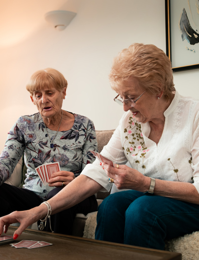 Two female residents enjoying a game of cards on the sofa in their apartment 