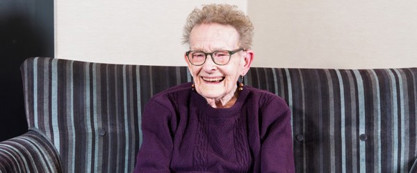 Resident sitting down on a sofa with a hot drink smiling