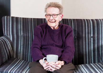 Resident sitting down with a hot drink smiling