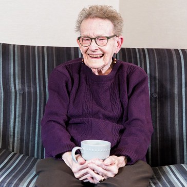 Resident sitting down with a hot drink smiling