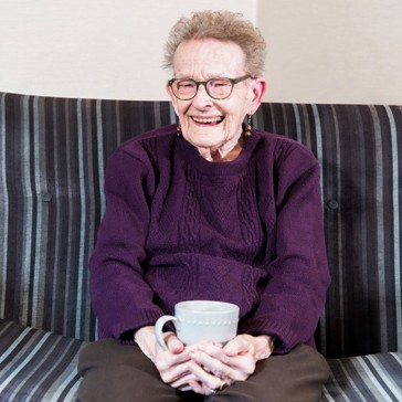 Resident sitting down on a sofa with a hot drink smiling