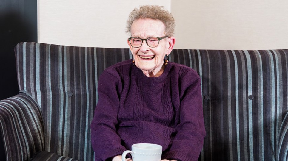 Resident sitting down with a hot drink smiling