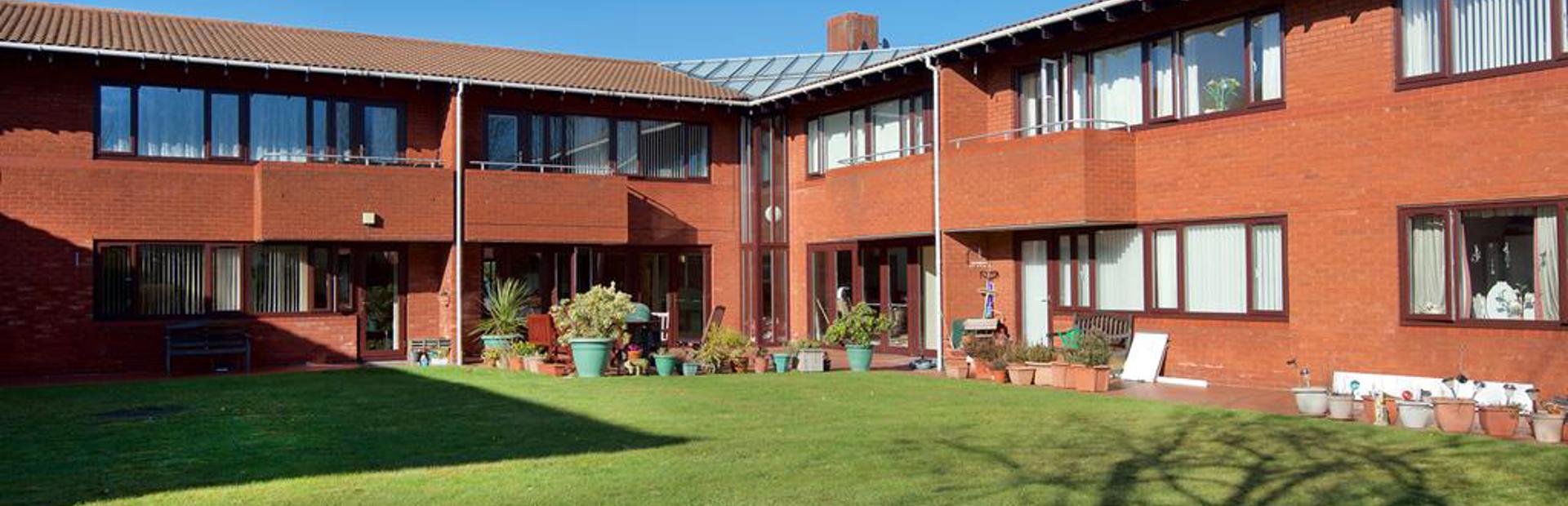 Large communal grassed area with plant pots around the outside alongside pathway