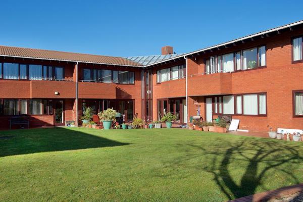Large communal grassed area with plant pots around the outside alongside pathway