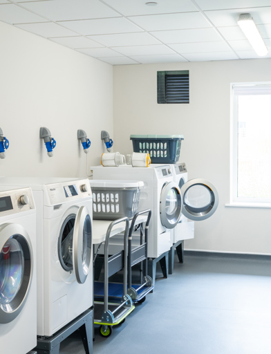 Communal laundry room with large tumble dryers and washing machines 
