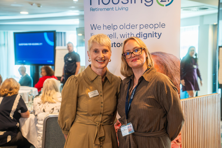 Two female Housing 21 colleagues standing at the conference and smiling