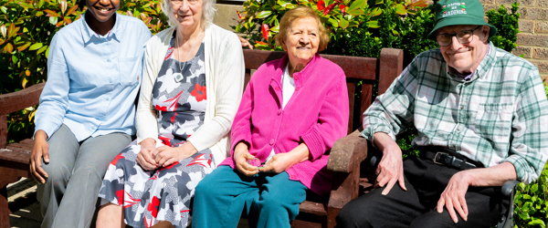 Three residents and a colleague sat on a garden bench on a sunny day