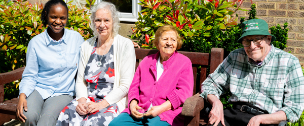 Three residents and a colleague sat on a garden bench on a sunny day