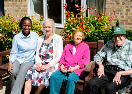 Three residents and a colleague sat on a garden bench on a sunny day
