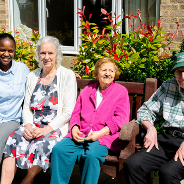 Three residents and a colleague sat on a garden bench on a sunny day